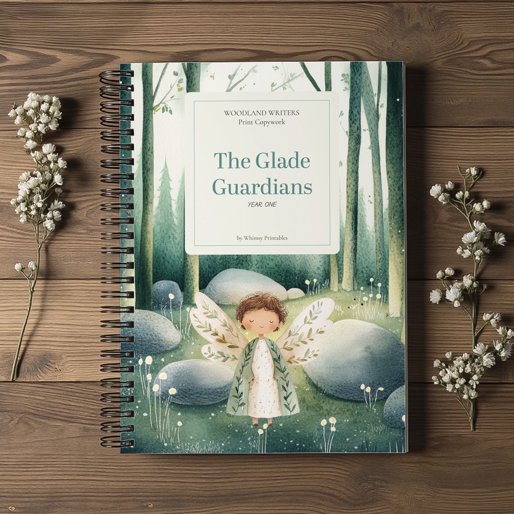 A spiral-bound book titled "The Glade Guardians" by William Froufables lies flat on a rustic wooden surface, surrounded by small white flowers. The cover features an illustration of a winged fairy in a green woodland scene.