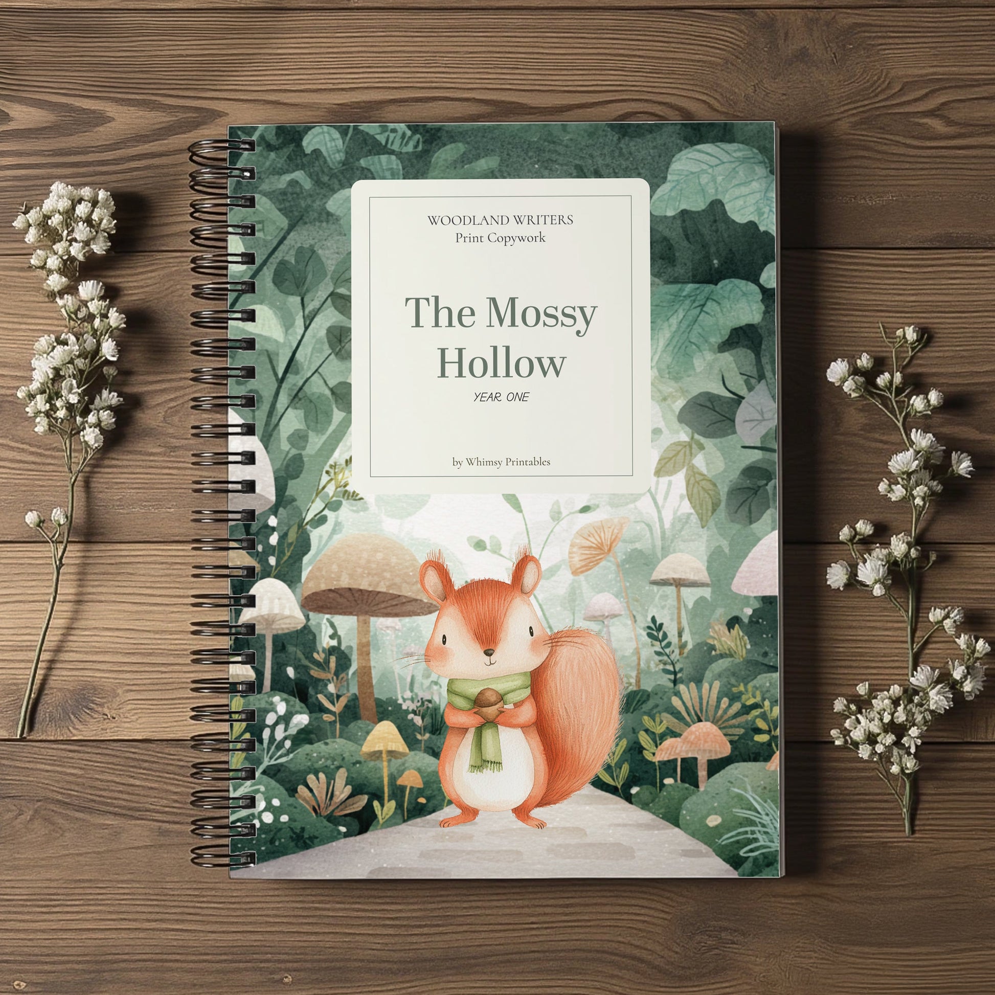 A spiral-bound children's book titled "The Mossy Hollow" by Whimsical Writers, featuring a forest illustration with a squirrel on the cover, styled on a wooden surface with dried white flowers.