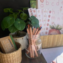Load image into Gallery viewer, Desk with jars of colored pencils, a plant, and educational materials on a wooden surface.

