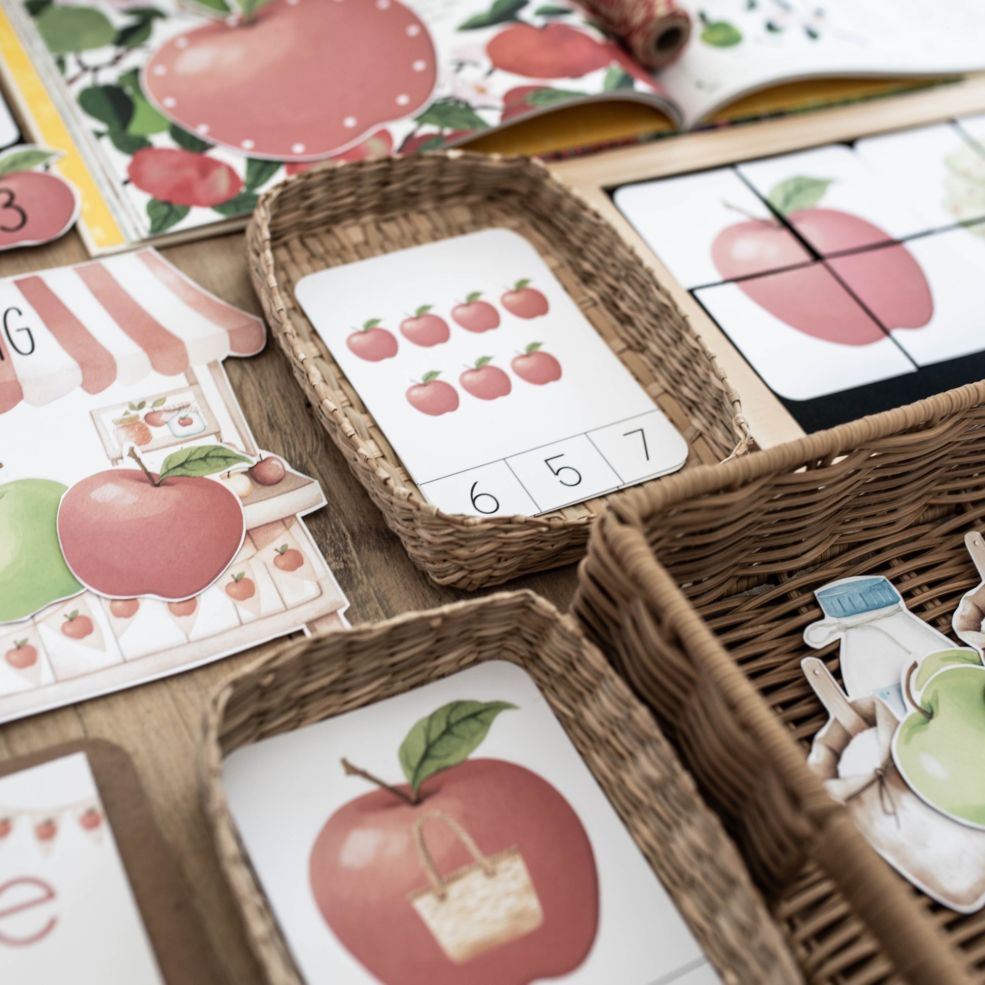 A close-up of children's educational play materials featuring red apples, numbers, and letters, arranged in woven baskets on a wooden surface.