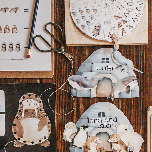 A collection of printable learning activities related to Arctic animals, laid out on a wooden surface. Activities include cutting and lacing cards, puzzles, and coloring pages.