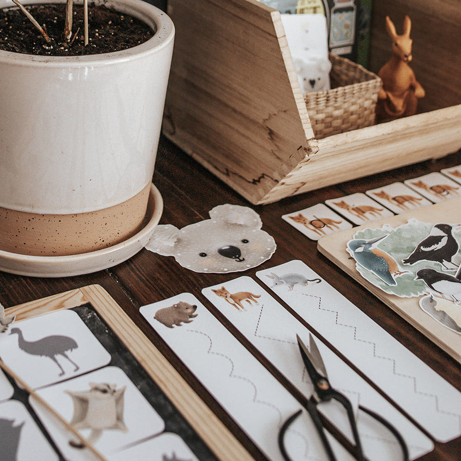 Educational morning basket with Australian animal-themed printables, toys, and a potted plant on a wooden table.