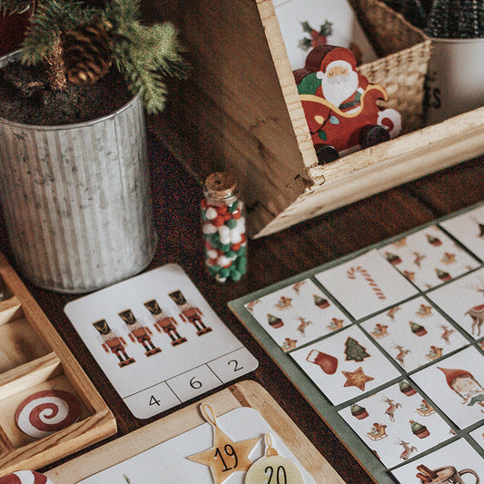 A Christmas morning basket setup with various holiday-themed items including cards, a memory game, and decorative elements on a wooden table.