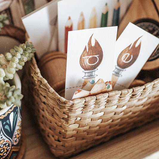 A digital product for visual arts education, featuring a PDF file with various learning activities such as flash cards, puzzles, and coloring sheets, displayed in a physical wicker basket alongside a plant and a spinning color wheel.